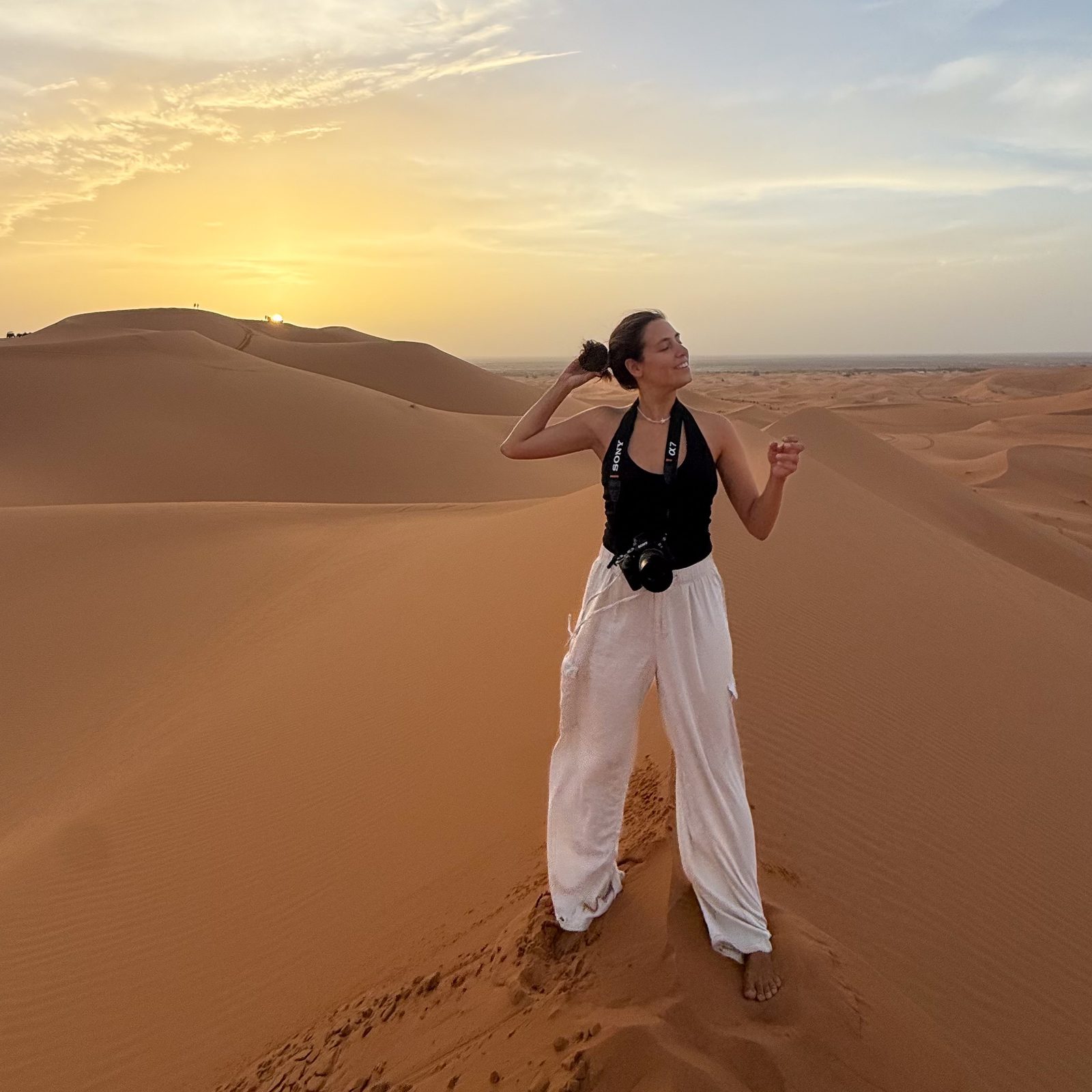 Belén Grachot barefoot on a sand dune at sunset, her camera around her neck